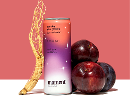 Moment energy drink can with a purple gradient, surrounded by a sprig of ginseng and plums on a pink background.